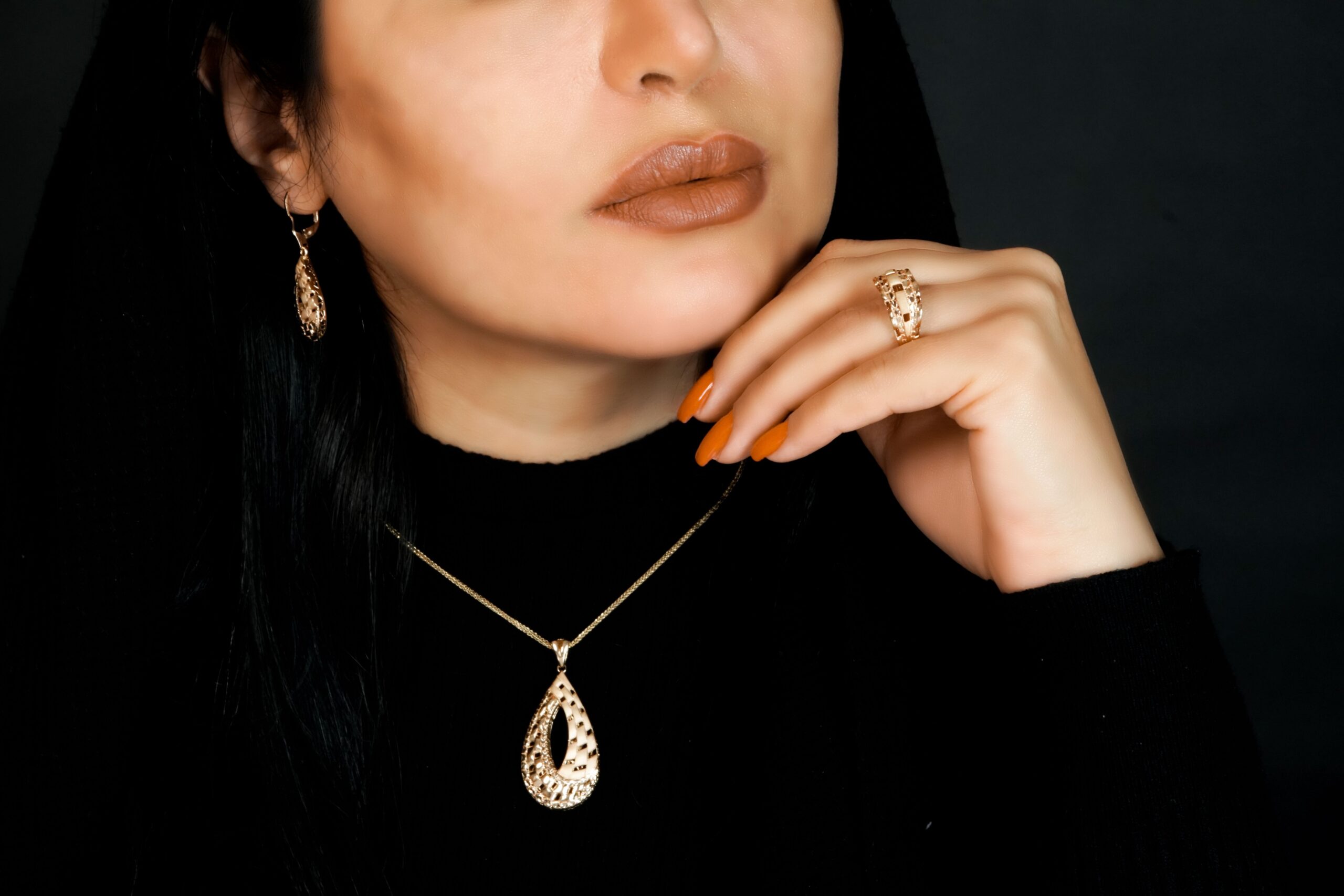 Home Close-up of a woman adorned in an elegant gold jewelry set, featuring a necklace, earrings, and ring.