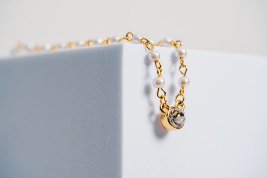 Home Close-up of a luxurious gold and pearl necklace delicately draped on a white block.