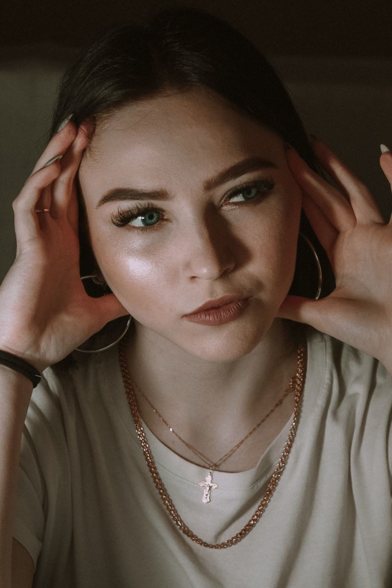 Home Portrait of a thoughtful young woman with green eyes and jewelry, under soft lighting.
