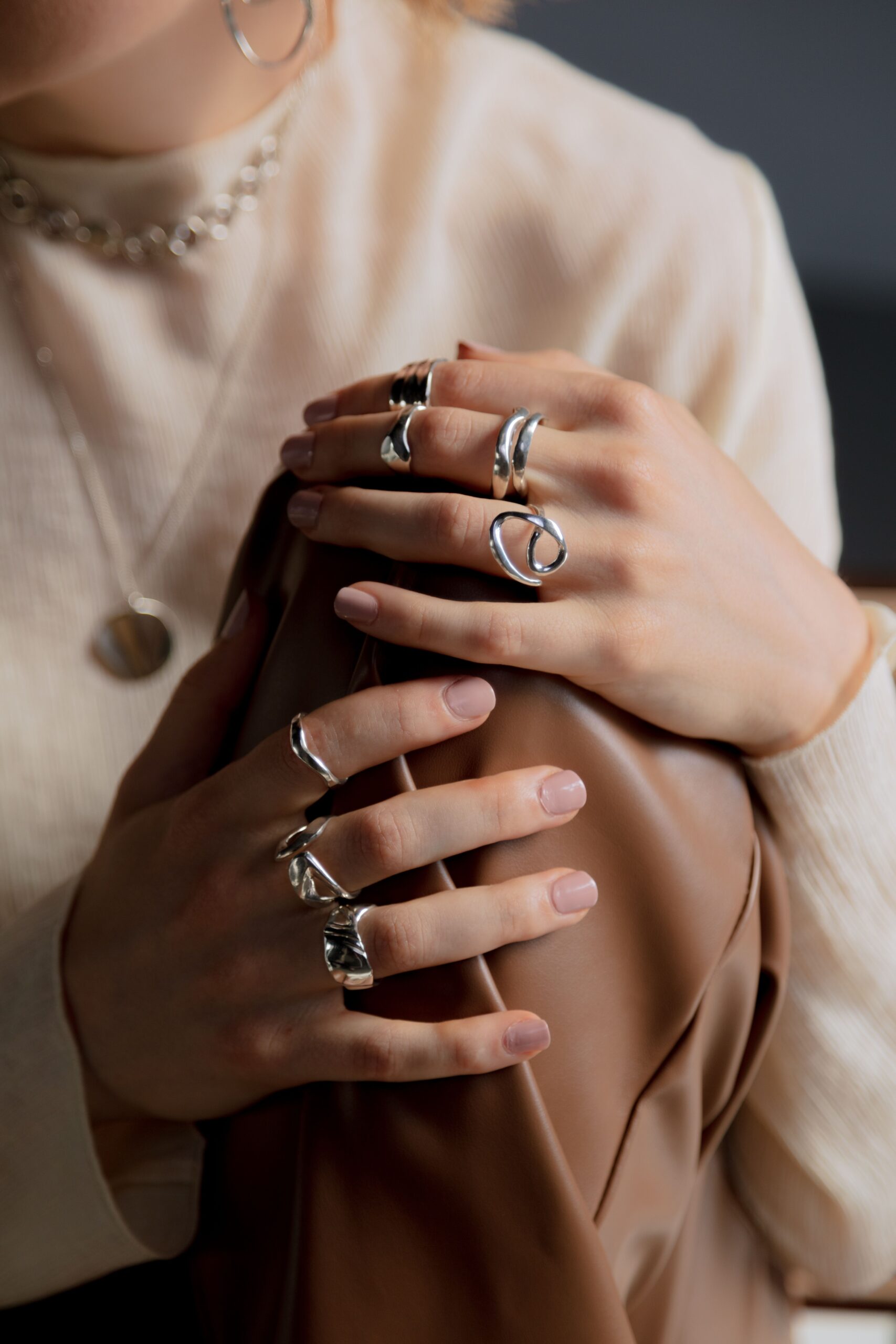 Home Close-up of elegant hands holding a leather material, adorned with stylish silver rings.